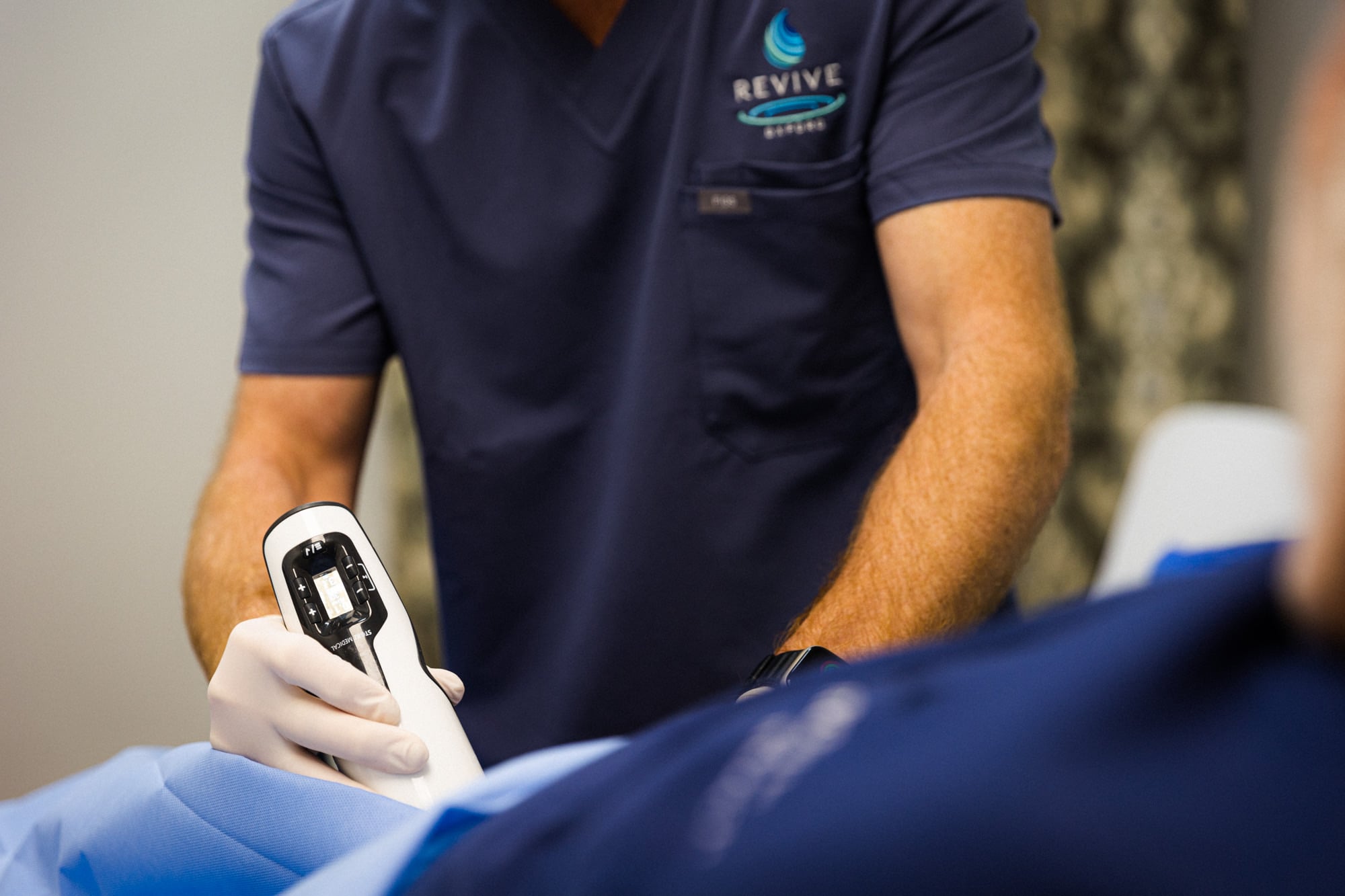 Healthcare provider at Revive Wellness performing focused shockwave therapy treatment on a patient's lower body using a handheld shockwave device to help relieve pain and promote healing.