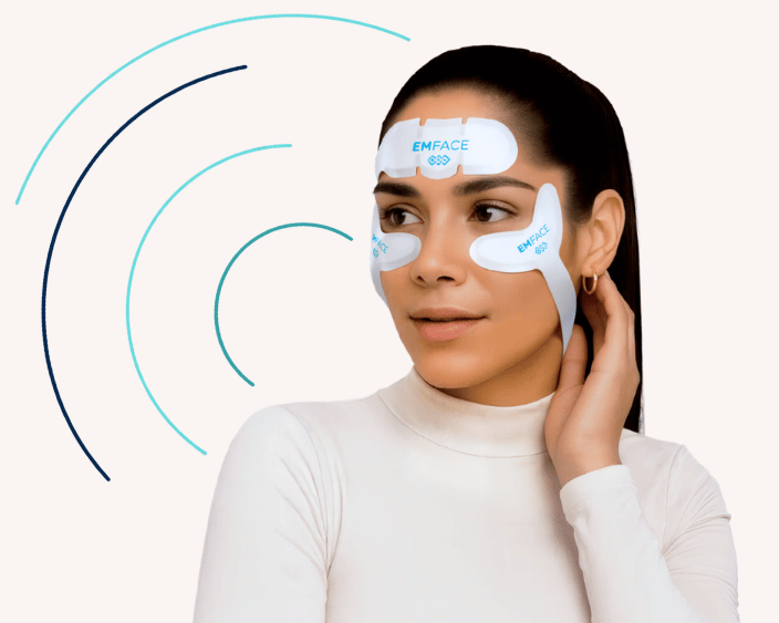 A woman wearing EMFACE facial treatment applicators on her forehead and cheeks, with her hand resting near her neck. Abstract curved lines in teal and navy surround her against a light background.