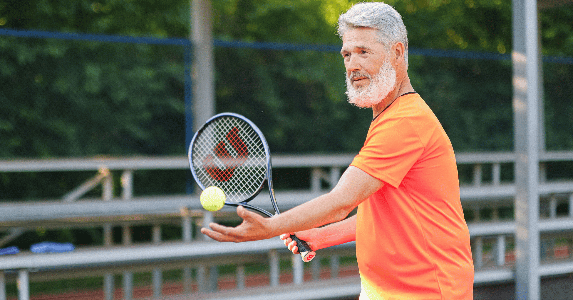 Older man playing tennis outdoors, holding a racket as he prepares to hit the ball.