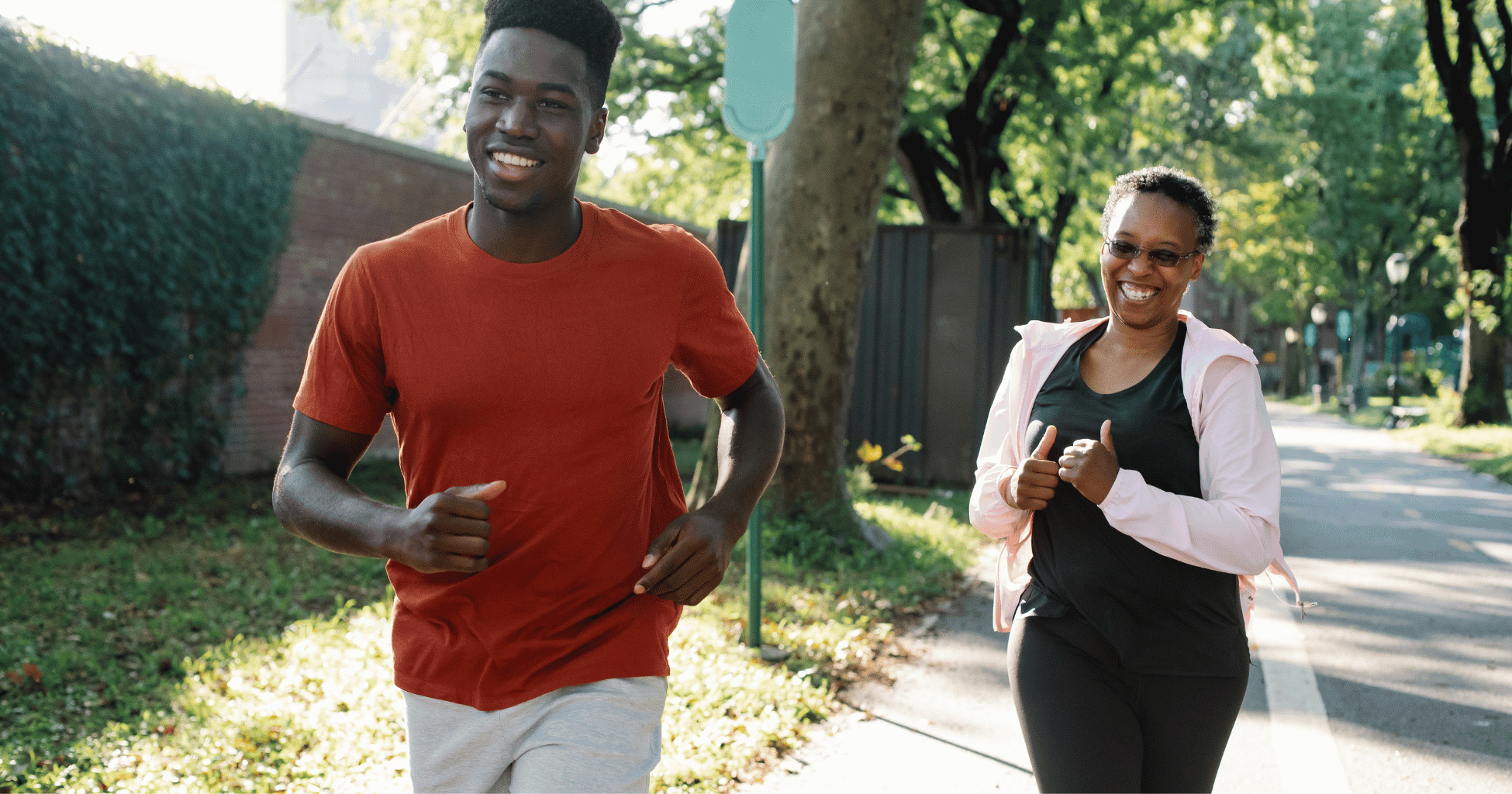 Two people smiling while jogging together outdoors on a sunny path.