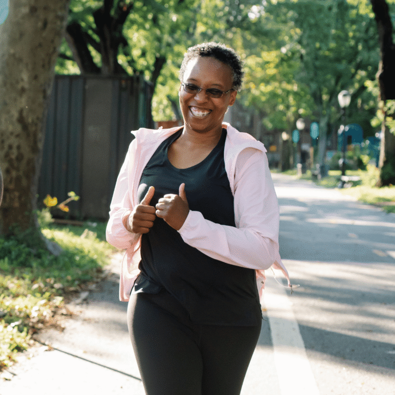 An older woman smiles while jogging outdoors on a sunny path.
